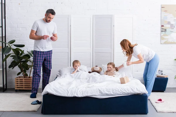 Батьки доглядають за хворими дітьми в спальні — стокове фото