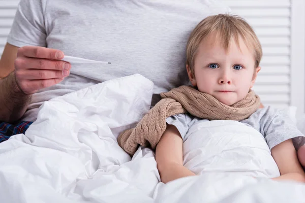 Geschnittenes Bild eines Vaters, der sich im Schlafzimmer um seinen kranken Sohn kümmert und seine Temperatur mit dem Thermometer überprüft — Stockfoto