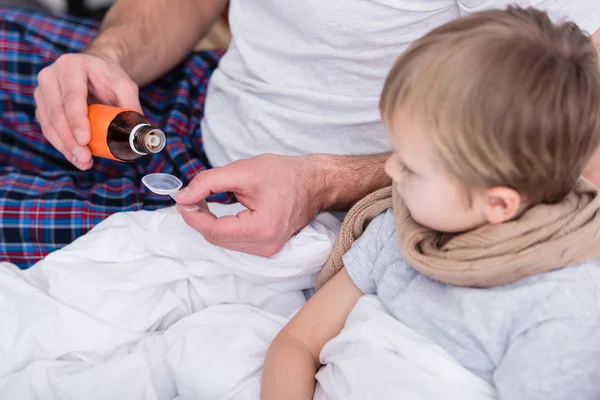 Geschnittenes Bild von Vater, der sich im Schlafzimmer um kranken Sohn kümmert und Medikamente in Löffel gießt — Stockfoto