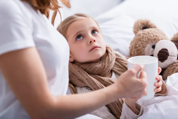 Imagen recortada de la madre cuidando a la hija enferma en el dormitorio y dándole una taza de té - foto de stock