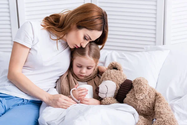 Mère prenant soin de sa fille malade et la serrant dans sa chambre — Photo de stock