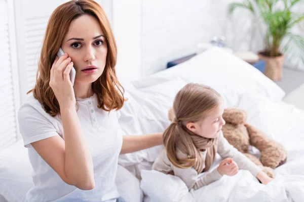 Verängstigte Mutter telefoniert per Smartphone mit Arzt, kranke Tochter im Bett — Stockfoto