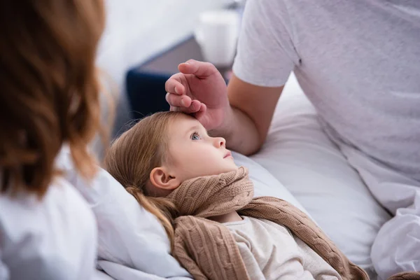 Immagine ritagliata dei genitori che si prendono cura della figlia malata in camera da letto, padre che le tocca la fronte — Foto stock