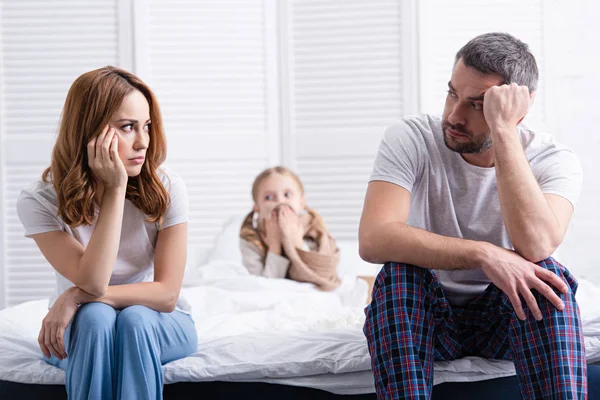 Besorgte Eltern sitzen neben kranker Tochter im Schlafzimmer und schauen einander an — Stockfoto