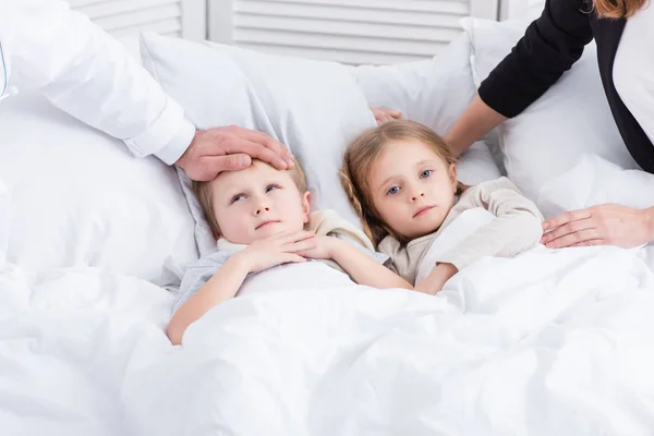 Imagen recortada de pediatra y madre cuidando niños enfermos en el dormitorio - foto de stock