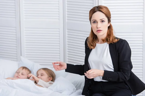 Besorgte Mutter steht neben zwei kranken Kindern und blickt im Schlafzimmer in die Kamera — Stockfoto