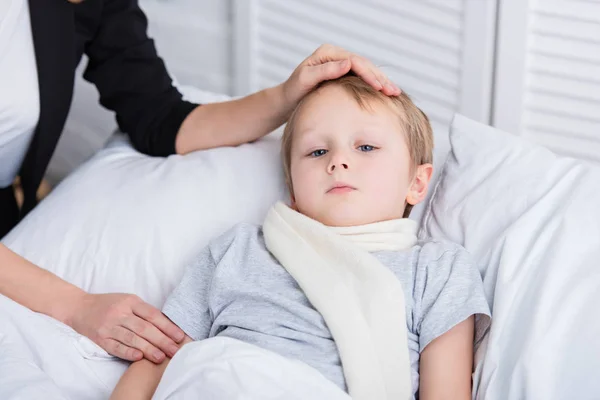 Immagine ritagliata di madre prendersi cura del figlio malato e toccare la fronte in camera da letto — Foto stock