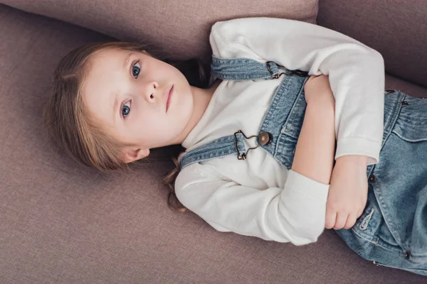 High angle view of sick child with stomach pain lying on sofa in living room and looking at camera — Stock Photo