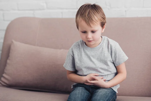 Sick boy with stomach pain sitting on sofa in living room — Stock Photo