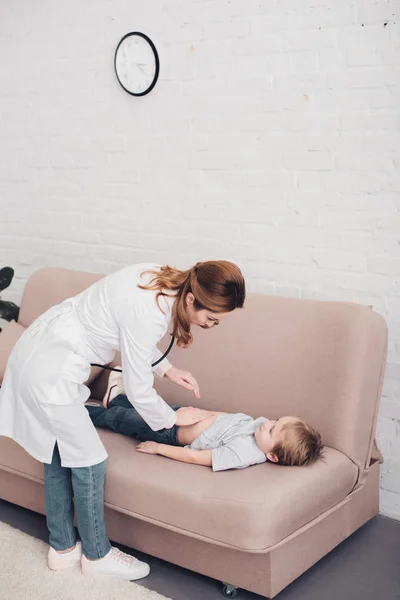 High angle view of pediatrist palpating sick boy stomach on sofa in living room — Stock Photo