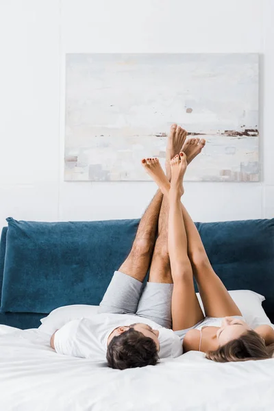 Joven novio y novia acostado en la cama blanca con las piernas levantadas - foto de stock