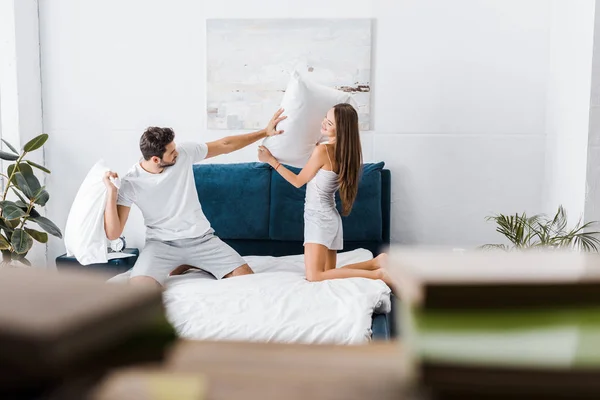 Enfoque selectivo de pareja joven teniendo pelea de almohadas en el dormitorio - foto de stock