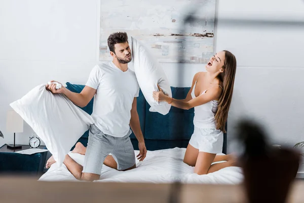 Enfoque selectivo de feliz pareja joven teniendo pelea de almohadas en la cama - foto de stock