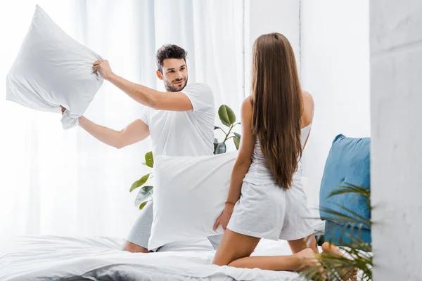 Bonito sorrindo homem ter travesseiro luta com namorada na cama — Fotografia de Stock