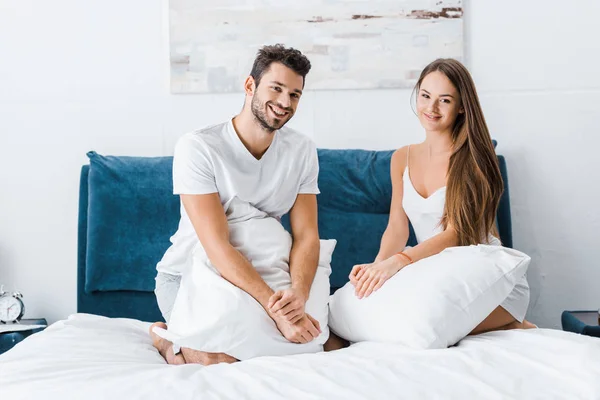 Young attractive couple sitting in bed with white pillows — Stock Photo