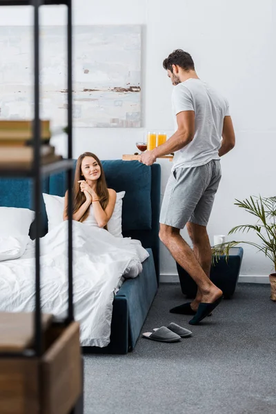 Young man giving tray with breakfast to girlfriend in bed — Stock Photo