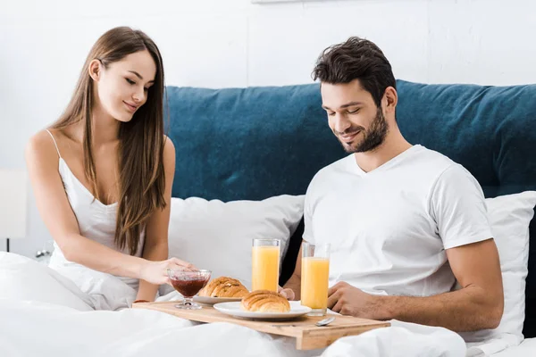 Young couple sitting in bed with breakfast on wooden tray — Stock Photo