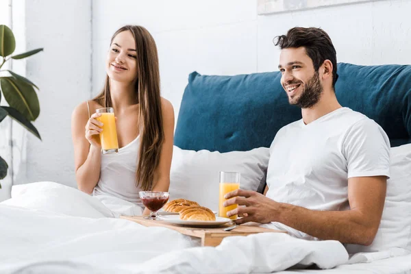 Jovem casal alegre tomando café da manhã na cama juntos — Fotografia de Stock