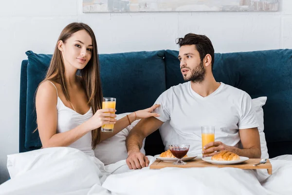 Young woman holding glass of orange juice and touching boyfriend in bed — Stock Photo