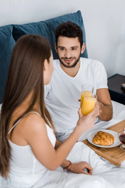 Handsome man looking at girlfriend and clinking with glasses of orange juice — Stock Photo