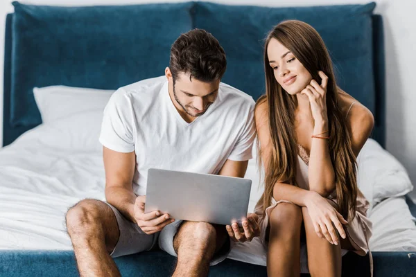 Jovem casal em pijama usando laptop no quarto — Fotografia de Stock