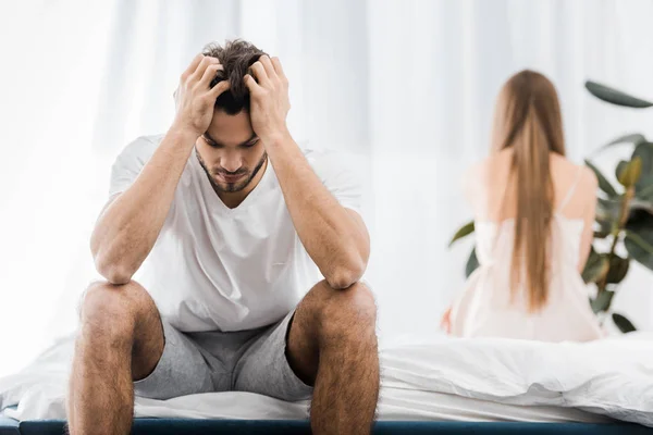 Depressed man with hands on head having sexual problems while sitting on bed with girlfriend — Stock Photo