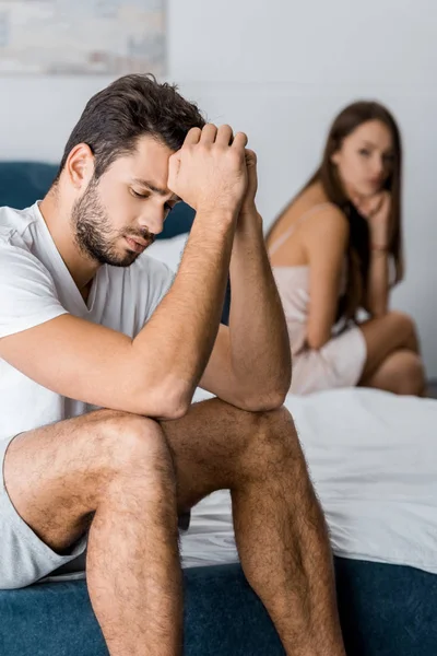 Расстроен мужчина с руками возле головы сидя на кровати с подругой после ссоры, сексуальные проблемы концепции — стоковое фото