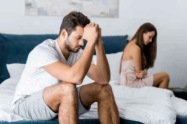 Hombre deprimido sentado en la cama con la novia después de la pelea, concepto de problemas sexuales - foto de stock