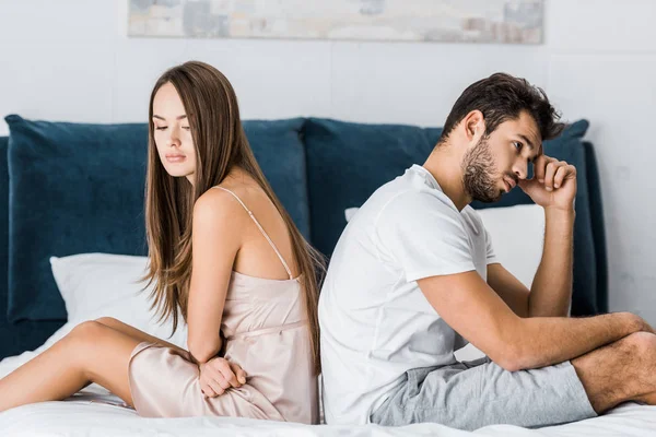 Jovem casal deprimido em pijama sentado na cama — Fotografia de Stock