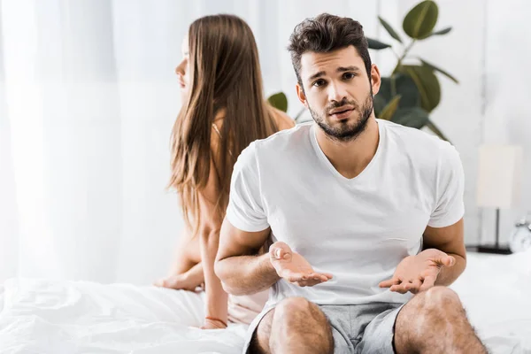 Young frustrated man having sexual problems while sitting on bed next to girlfriend — Stock Photo