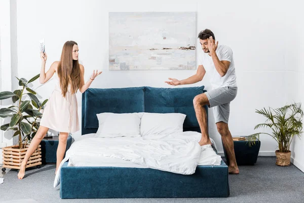 Jovem casal zangado de pé perto da cama e brigando no quarto — Fotografia de Stock