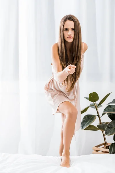 Young angry girl standing on bed and pointing with finger at camera — Stock Photo