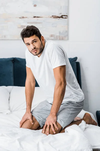 Junger gutaussehender verwirrter Mann sitzt schlecht gelaunt im Bett — Stockfoto