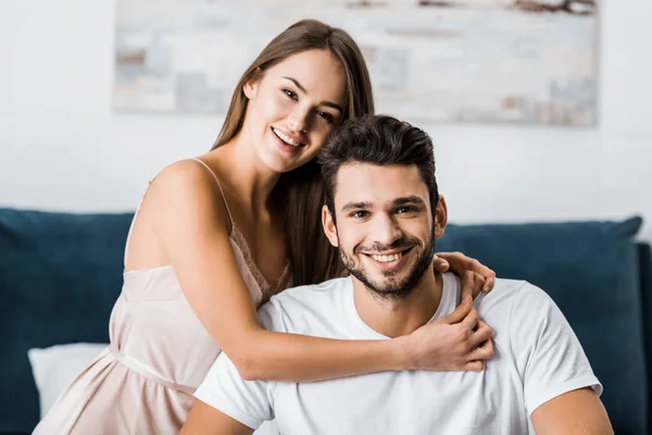 Молодая привлекательная женщина обнимает парня и улыбается, сидя на кровати — стоковое фото