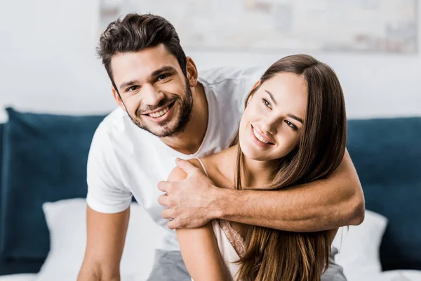 Young happy man hugging girlfriend and smiling cheerfully — Stock Photo