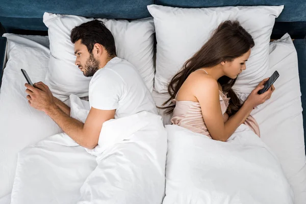 Vista superior de la joven pareja acostada en la cama por la mañana y utilizando teléfonos inteligentes - foto de stock