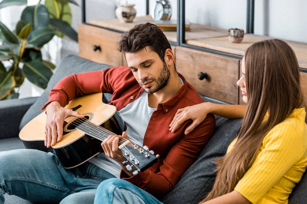 Giovane ragazza seduta sul divano con fidanzato mentre ascolta musica per chitarra — Foto stock