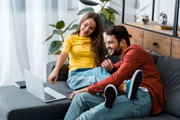 Young couple sitting on sofa while girl pointing with finger at laptop — Stock Photo
