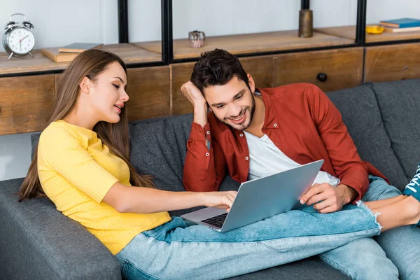 Jovem menina atraente mostrando algo no laptop para namorado sorridente — Fotografia de Stock