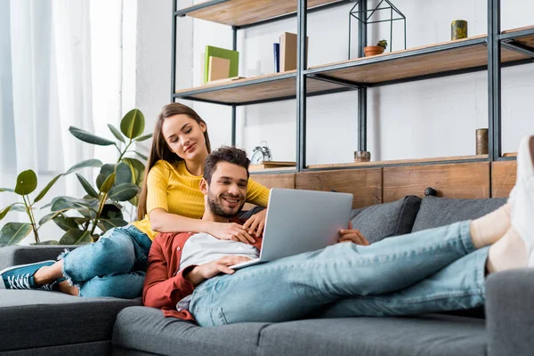 Joven feliz pareja descansando en el sofá con el ordenador portátil - foto de stock