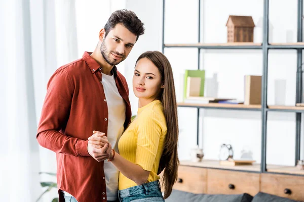 Enfoque selectivo de novio alegre y novia tomados de la mano en la sala de estar - foto de stock