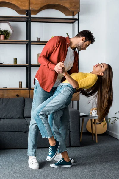 Bell'uomo barbuto che balla con la fidanzata attraente in soggiorno — Foto stock