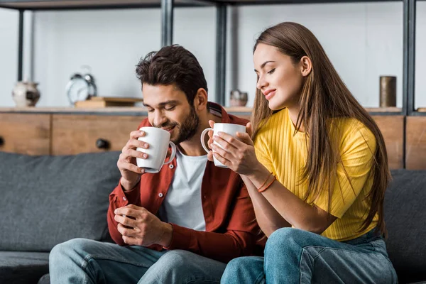 Fröhliche Freundin hält Tasse und sitzt neben Freund im Wohnzimmer — Stockfoto