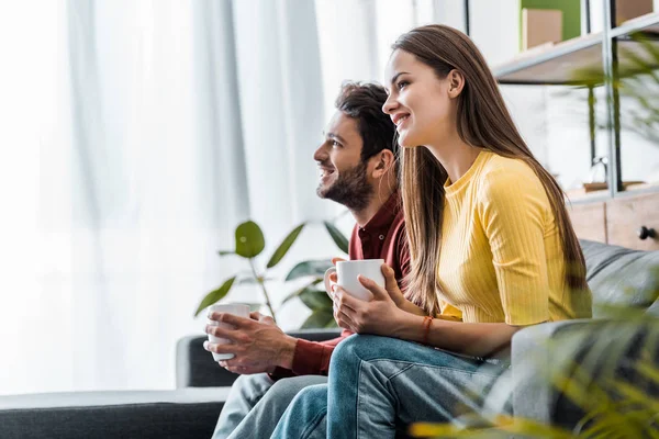 Attraktive Frau sitzt auf Sofa und hält Tasse neben Freund — Stockfoto