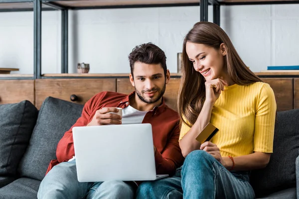 Alegre pareja haciendo compras en línea y sonriendo en el sofá — Stock Photo