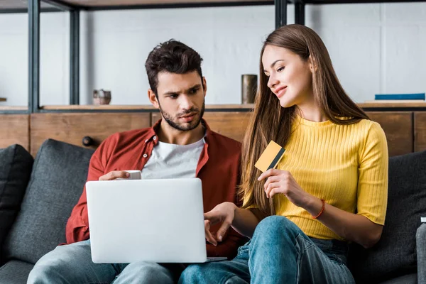 Attractive woman holding credit card while boyfriend sitting with laptop — Stock Photo