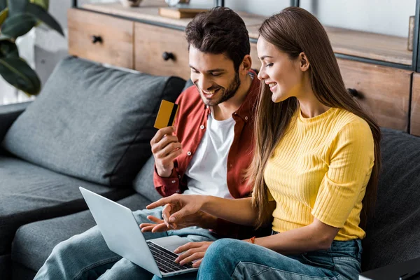 Счастливый мужчина, держащий кредитную карту и делающий онлайн-покупки рядом с подругой — стоковое фото