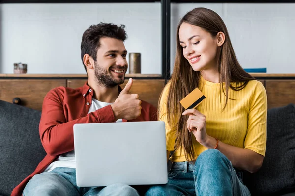 Happy woman holding credit card while boyfriend showing thumb up sign — Stock Photo