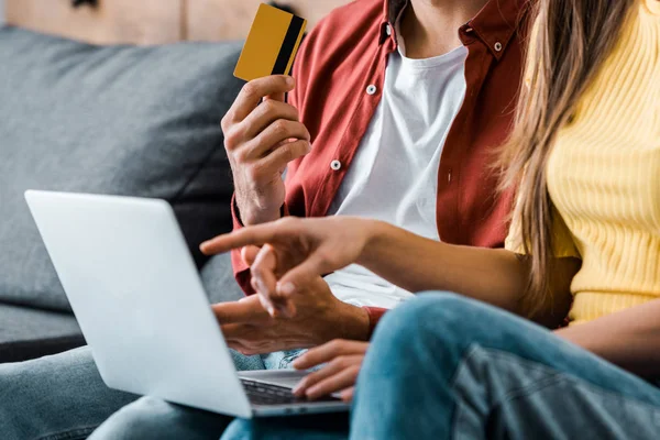 Recortado vista de hombre sosteniendo tarjeta de crédito y haciendo compras en línea cerca de novia - foto de stock