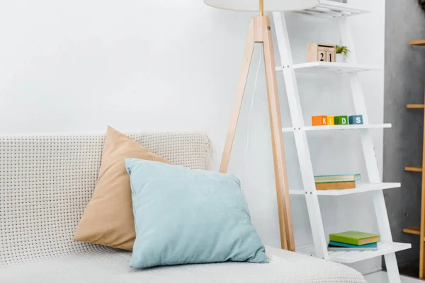 Modern pillows on sofa near wooden lamp and toys on rack — Stock Photo